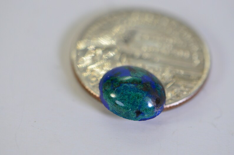 May include: A close-up of a green and blue oval-shaped gemstone, approximately the size of a US quarter.
