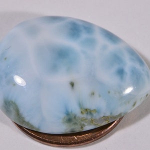 May include: A light blue cabochon gemstone with a white and blue marbled pattern. The gemstone is about the size of a US penny.