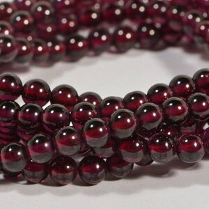 May include: A strand of deep red garnet beads. The beads are round and smooth, and they have a glossy finish.