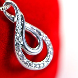May include: A silver pendant necklace with a double infinity symbol design, accented with small clear cubic zirconia stones.