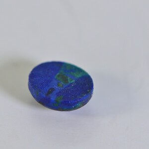 May include: A close-up of a blue and green oval-shaped gemstone. The gemstone has a rough, textured surface.