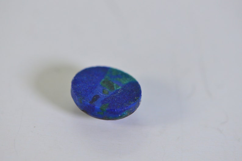 May include: A close-up of a blue and green oval-shaped gemstone. The gemstone has a rough, textured surface.