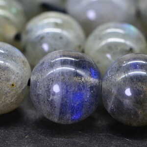 May include: A strand of round, grey labradorite beads with iridescent blue and green flashes. The beads are strung on a black cord.