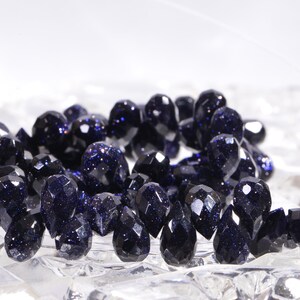 May include: A strand of dark blue faceted gemstone beads. The beads are teardrop shaped and have a sparkly, speckled appearance.