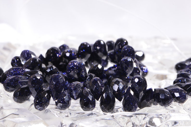May include: A strand of dark blue faceted gemstone beads. The beads are teardrop shaped and have a sparkly, speckled appearance.