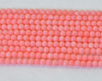 May include: A strand of small, round, smooth beads in a uniform light coral pink color. The beads are arranged in multiple parallel rows, showcasing a consistent spherical shape and a subtle, natural-looking matte finish across the entire collection.