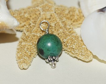 Puede incluir: Un colgante de piedra preciosa verde con una argolla de plata y una cuenta de plata decorativa en la parte inferior. El colgante se muestra en una estrella de mar y conchas marinas.