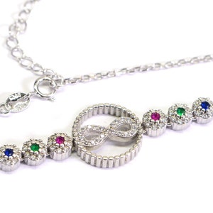 May include: Silver bracelet featuring an infinity symbol charm and four small round stones set in silver. The stones are red, green, blue, and clear.