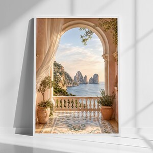 May include: A framed wall art print depicting a Mediterranean balcony with a stone balustrade, terracotta pots with green plants, and a sheer white curtain. The view through the arched opening shows the sea and rocky cliffs under a soft sky.