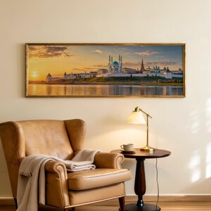 May include: A panoramic wall art print featuring the Kul Sharif Mosque in Kazan at sunset, displayed in a thin gold frame. The scene shows the white stone mosque with blue domes reflecting in the water under a warm, golden orange sky.