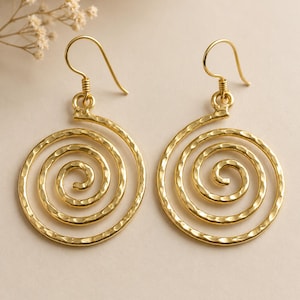 May include: A pair of gold spiral earrings. The earrings feature a hammered texture and a hook fastening. The design is a series of concentric circles, creating a spiral effect. The earrings are displayed on a neutral background.