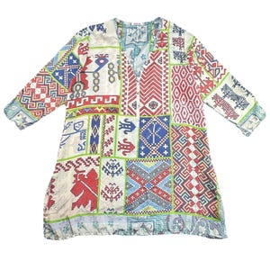 Puede incluir: Una túnica de manga larga con un diseño de patchwork. La túnica presenta un cuello en V y una variedad de patrones geométricos y florales en rojo, azul, verde y blanco. La túnica está hecha de una tela ligera.