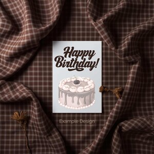 Peut inclure: Une carte de vœux avec le texte "Happy Birthday!" dans une police manuscrite. La carte présente une illustration d'un gâteau avec un glaçage blanc, un glaçage gris et une cerise sur le dessus. Les mots "Example Design" sont en bas.