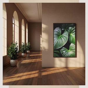 Può includere: Una stampa botanica incorniciata con grandi foglie verdi strutturate su sfondo scuro. L'immagine è esposta su una parete in una stanza con finestre ad arco, piante in vaso e pavimento in legno. La stanza è inondata di luce naturale.