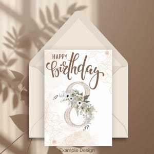 May include: A birthday card with the words "Happy Birthday" in elegant brown script. The number 8 is decorated with white flowers and greenery. The card is inside a cream-colored envelope, with a floral design on the card and envelope.