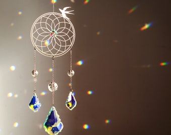 May include: A white dream catcher with a crystal bead design hangs from a ceiling with iridescent light reflecting off the crystals.