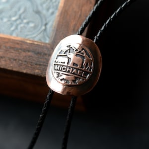May include: A copper bolo tie with a circular pendant featuring an elephant, giraffe, and other animals. The pendant also includes the name "MICHAEL" engraved on it.