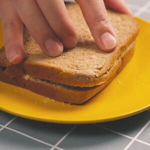 May include: A sandwich on a bright yellow plate. The sandwich is made with whole wheat bread and appears to have a filling. A hand is reaching for the sandwich.