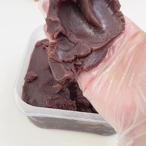 Puede incluir: Primer plano de un recipiente lleno de pasta de frijoles rojos oscuros. Se levanta una porción de la pasta, mostrando su textura suave. El fondo incluye un calendario de madera con la fecha "SEP 06".