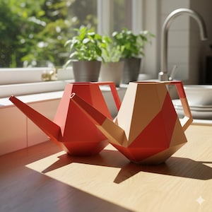 May include: Two geometric design watering cans. One is solid red, the other is beige and red. Both have long spouts and handles. They sit on a wooden surface in front of a window with plants.