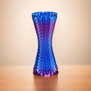 May include: A decorative vase with a unique design. The vase transitions from a deep blue at the top to a vibrant purple at the base. The surface features a textured, geometric pattern, adding visual interest to the piece.
