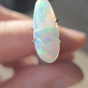 Peut inclure: Une pierre d'opale en forme de poire avec une base blanche et des éclairs irisés de vert, de bleu et d'orange. L'opale est maintenue par quatre griffes argentées. La pierre précieuse mesure environ 3,8 cm de long.