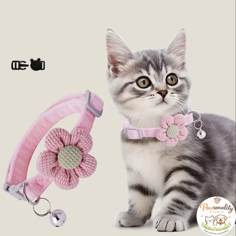 A gray and white tabby kitten sitting and looking forward, wearing the pink knit collar with the pink flower. The collar is made of soft material.