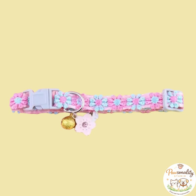 Pink and blue floral cat collar with a gold bell and a pink flower charm. The collar has a plastic buckle and a metal D-ring. The collar laid out flat horizontally, showing the adjustable strap, bell and flower bell attachment