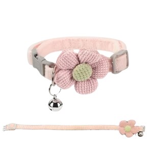 Pink cat collar with a large, knitted flower and a small silver bell. The collar has a gray plastic buckle and a matching flower on the end. The collar is made of a soft, plush material.