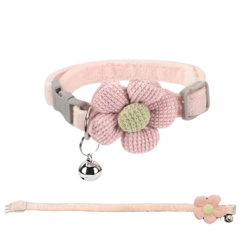 Pink cat collar with a large, knitted flower and a small silver bell. The collar has a gray plastic buckle and a matching flower on the end. The collar is made of a soft, plush material.