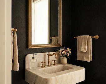 May include: A luxurious bathroom vanity with a marble sink, gold fixtures, and a matching mirror. The dark walls provide a striking contrast to the light-coloured sink and towels. A gold light fitting is mounted above the mirror.