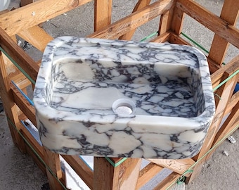 May include: A rectangular marble sink with a white and grey veined pattern. The sink has a single drain hole and is set inside a wooden crate. The sink is a bathroom fixture.