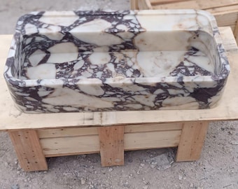 May include: A rectangular marble sink with a white and dark purple patterned design. The sink is placed on a wooden stand made of light brown planks. The sink is a bathroom fixture.