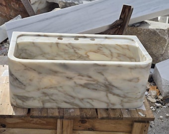 May include: A white ceramic mug with a black handle and the text "But First, Coffee" in a bold, black font. The mug is set against a blurred background, suggesting a cosy setting.