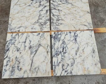 May include: Four rectangular marble tiles with a white base and detailed veining in grey and gold hues. The tiles are placed together, displaying the natural patterns and textures of the stone. Each tile is approximately 60 cm x 60 cm.