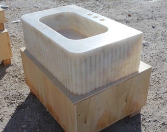 May include: An off-white marble sink with a rectangular basin and three tap holes, set on a wooden crate. The sink's front features vertical ribbed detailing. The sink's dimensions are approximately 76 cm in length.