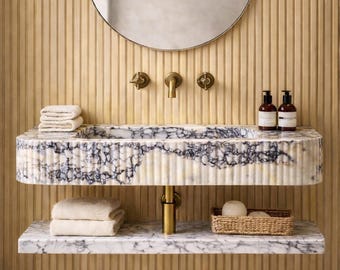 May include: A contemporary bathroom featuring a marble sink with a blue and white pattern, mounted on a gold support. A round mirror is above the sink, and the wall has vertical wooden panels. The sink has a shelf below it.