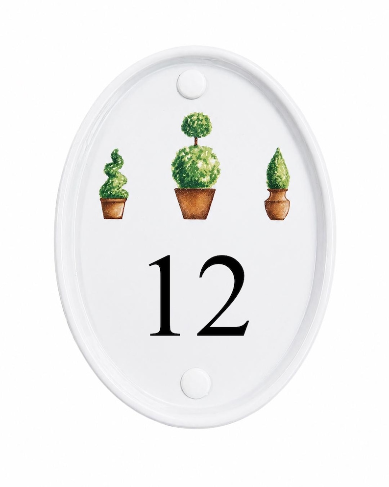 May include: White oval house number sign with the number 12 in black. The sign features three watercolor illustrations of potted topiary plants in shades of green and brown. Two white fasteners are at the top and bottom.