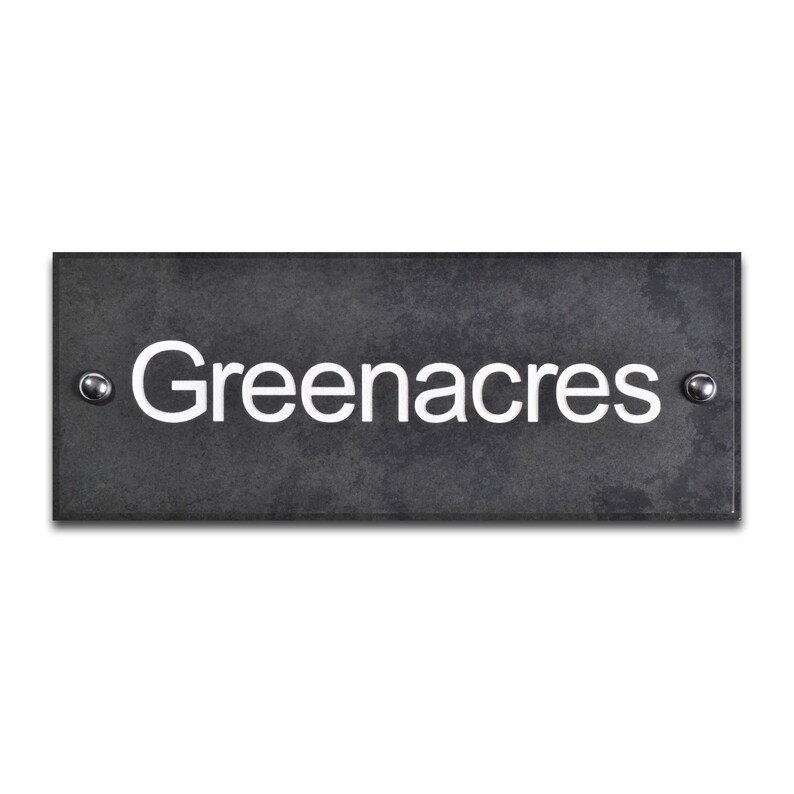 May include: A rectangular, dark grey slate house sign. The name "Greenacres" is displayed in a white, sans-serif font. The sign is fixed with two silver screws, one on each side.