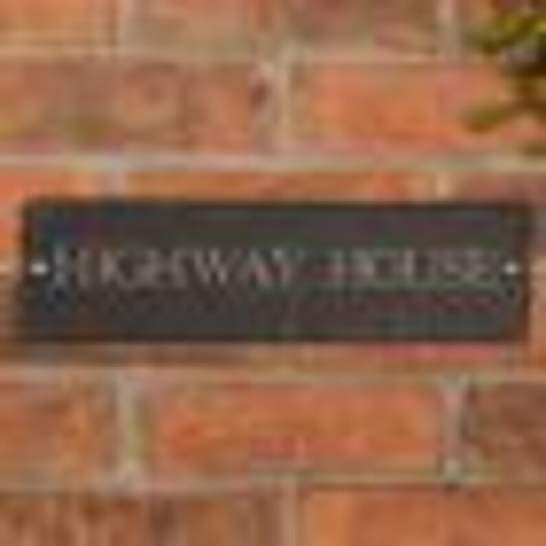 May include: A rectangular, dark gray slate sign with the text "HIGHWAY HOUSE" in white lettering. The sign is mounted on a red brick wall, with the text centered horizontally.