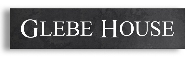 May include: A rectangular sign with the words "GLEBE HOUSE" in white, sans-serif font. The sign has a dark grey, textured background, and a subtle shadow.