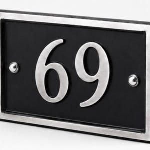 Puede incluir: Placa rectangular negra con el n&uacute;mero 69 en plata. La placa tiene un borde plateado y dos remaches plateados. Un letrero de n&uacute;mero de casa moderno y elegante.