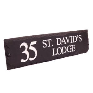 May include: A rectangular black slate house sign with white lettering. The sign reads "35 ST. DAVID'S LODGE". The numbers and text are in a bold, sans-serif font. The slate has a natural, textured surface.