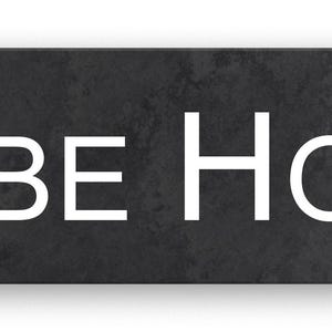 May include: A rectangular, dark grey sign with the words "GLEBE HOUSE" in large, white, sans-serif font. The sign has a textured appearance and a subtle shadow.