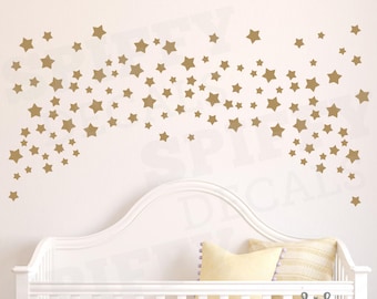 May include: A white crib with a gold star decal on the wall above it. The decal is in the shape of a shooting star with many smaller stars trailing behind it. The text "spiffy decals" is in the lower right corner of the image.
