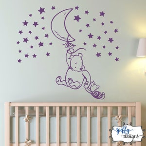 Puede incluir: Pegatina de pared de Winnie de Pooh y Piglet de color morado con un globo en forma de media luna y estrellas. La pegatina est&aacute; en una pared verde claro sobre una cuna blanca.