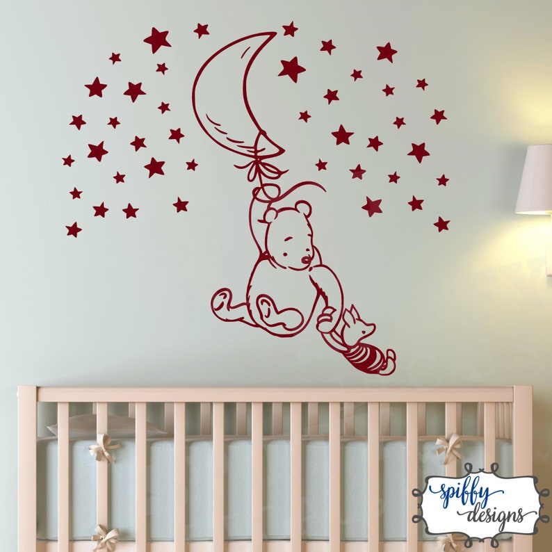 Puede incluir: Pegatina de pared roja de Winnie de Pooh y Piglet con un globo en forma de media luna y estrellas. La pegatina est&aacute; en una pared verde claro sobre una cuna blanca.