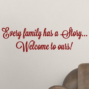 May include: A red cursive font wall decal with the text "Every family has a story... Welcome to ours!"