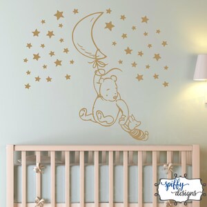 Puede incluir: Una calcoman&iacute;a de pared de Winnie de Pooh y Piglet que representa a Winnie de Pooh sujetando un globo en forma de media luna y Piglet sujetando la cola de Winnie. La calcoman&iacute;a es de color dorado y est&aacute; rodeada de una dispersi&oacute;n de estrellas doradas.
