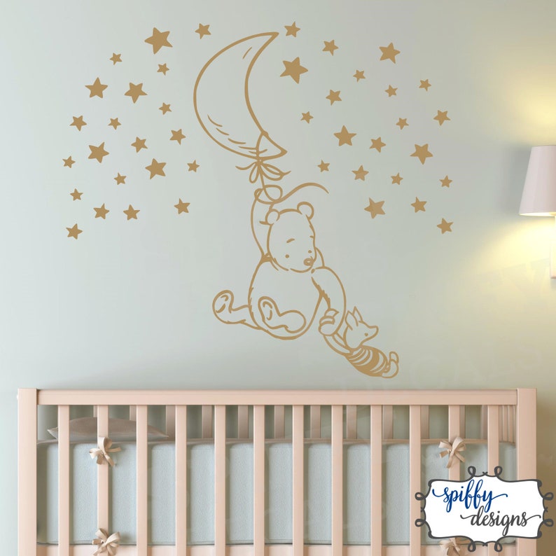 Puede incluir: Una calcoman&iacute;a de pared de Winnie de Pooh y Piglet que representa a Winnie de Pooh sujetando un globo en forma de media luna y Piglet sujetando la cola de Winnie. La calcoman&iacute;a es de color dorado y est&aacute; rodeada de una dispersi&oacute;n de estrellas doradas.